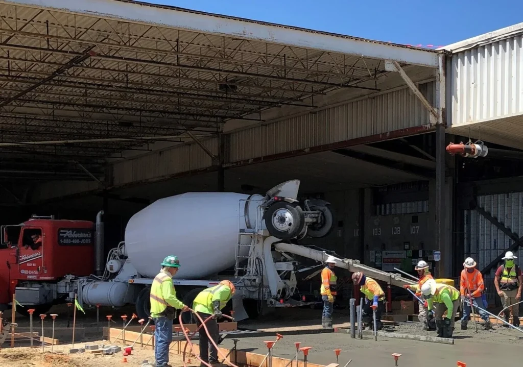Crew placing a concrete slab from a mixer truck inside an open-sided building
