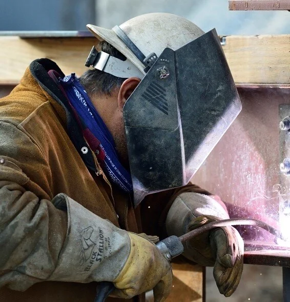 Welder in a welding helmet and leathers working on structural steel